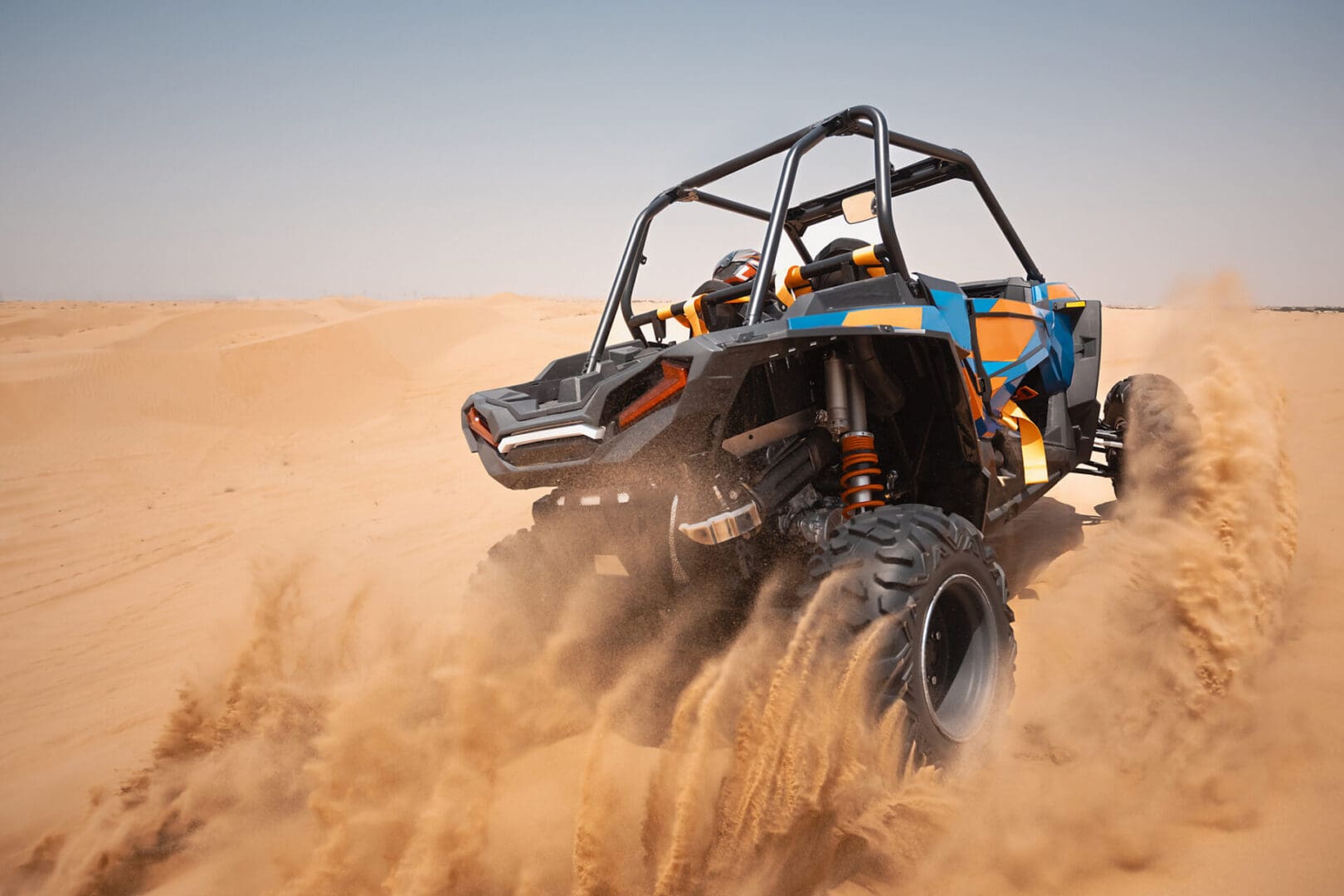 Blue and orange UTV kicking sand